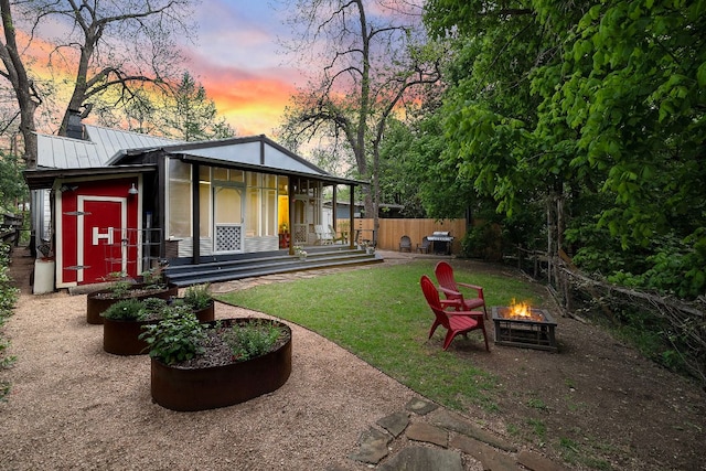 back of house at dusk with metal roof, an outdoor fire pit, fence, a lawn, and a standing seam roof