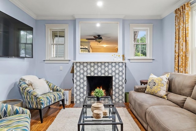 living area with ceiling fan, crown molding, a tiled fireplace, and wood finished floors