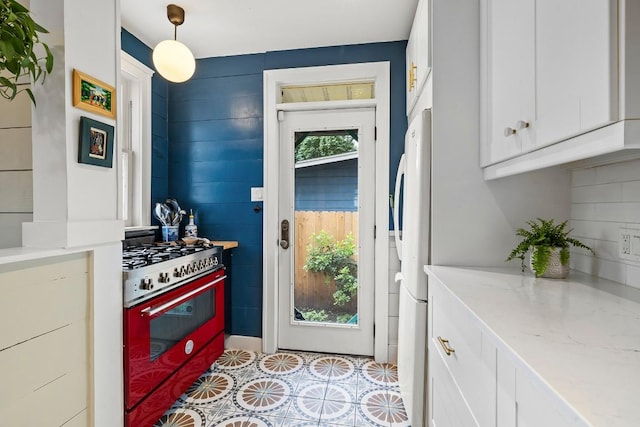 kitchen featuring backsplash, freestanding refrigerator, white cabinetry, light stone countertops, and gas range