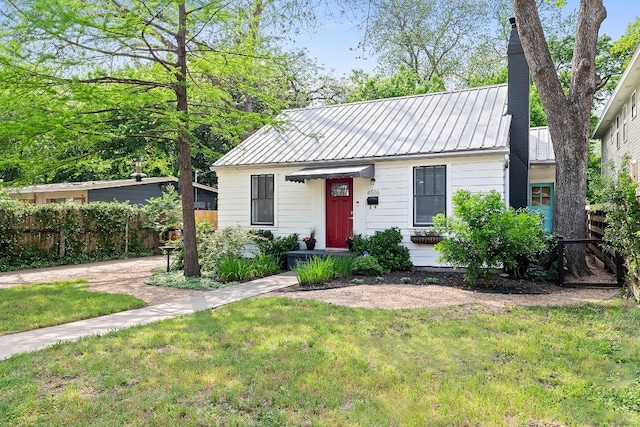 view of front of property with metal roof, fence, a chimney, and a front lawn