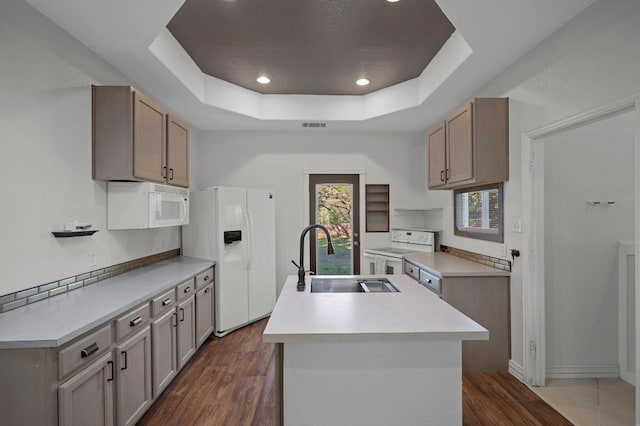 kitchen featuring dark wood-type flooring, a raised ceiling, white appliances, and a sink