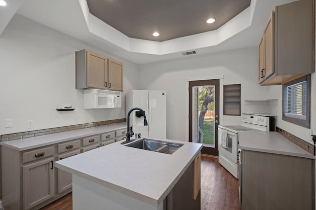 kitchen with white appliances, a sink, visible vents, a tray ceiling, and dark wood finished floors