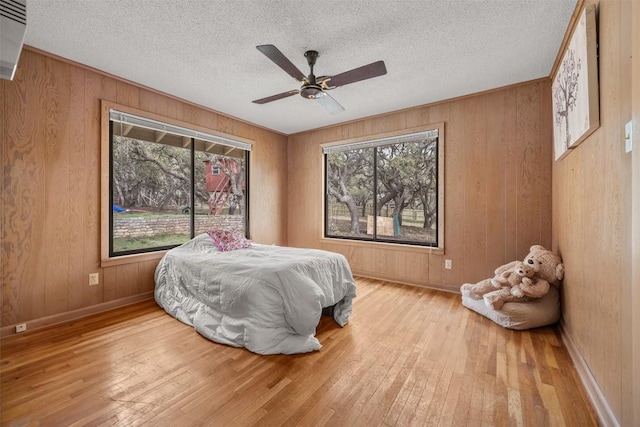1876 Rocky Rd, Blanco, TX 78606 - bedroom featuring multiple windows, hardwood / wood-style floors, wood walls, a ceiling fan, and a textured ceiling
