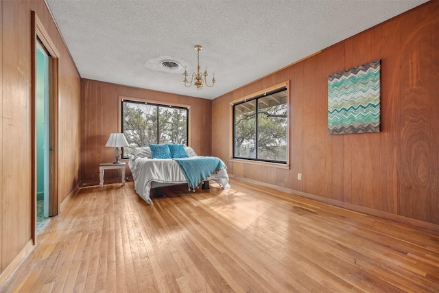 1876 Rocky Rd, Blanco, TX 78606 - bedroom with light wood-style floors, a chandelier, a textured ceiling, and wooden walls
