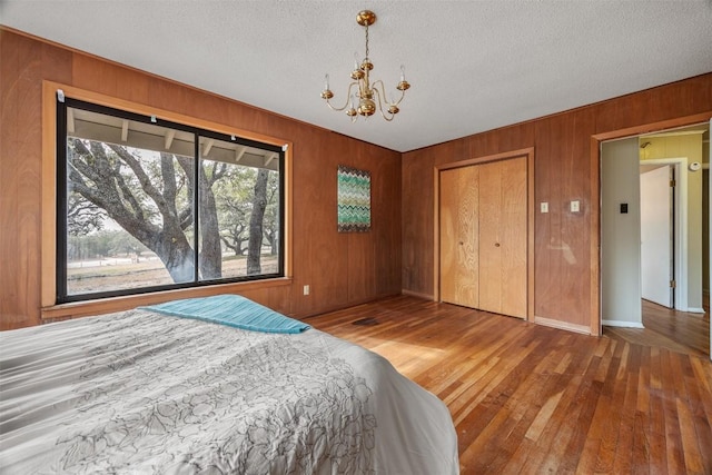 1876 Rocky Rd, Blanco, TX 78606 - bedroom with a chandelier, wood-type flooring, wooden walls, a closet, and a textured ceiling