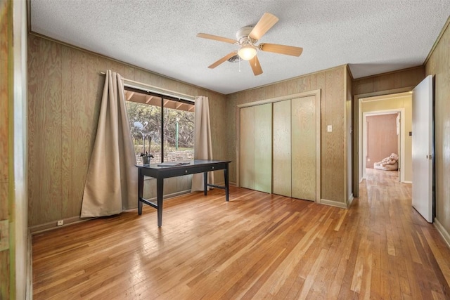 1876 Rocky Rd, Blanco, TX 78606 - bedroom with light wood finished floors, wood walls, a closet, a textured ceiling, and ceiling fan