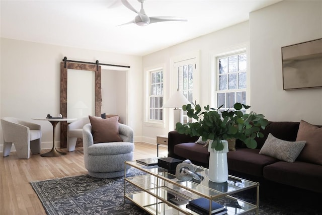 living area with a barn door, baseboards, ceiling fan, and wood finished floors