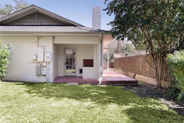 back of property featuring a yard, a chimney, fence, and brick siding