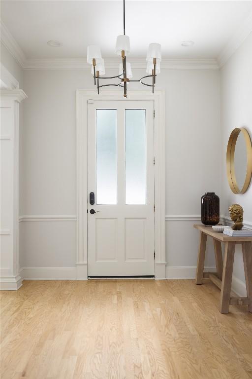 entryway with light wood-style floors, a notable chandelier, baseboards, and crown molding