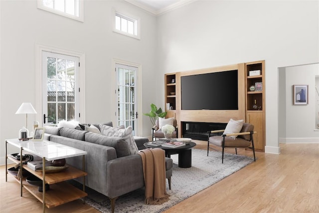 living area featuring built in features, baseboards, ornamental molding, wood finished floors, and a high ceiling