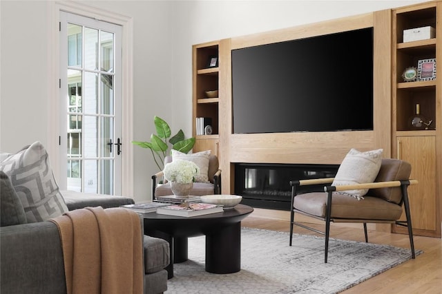 sitting room featuring built in shelves, a fireplace, and wood finished floors