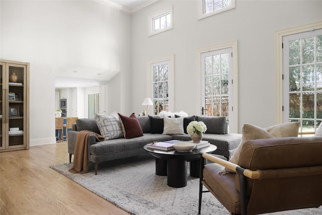 living room with light wood-style floors, ornamental molding, a towering ceiling, and baseboards