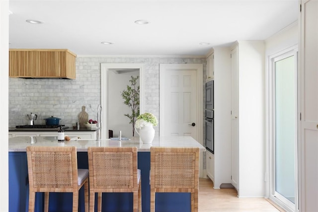 kitchen with tasteful backsplash, ornamental molding, oven, light wood-type flooring, and gas stovetop