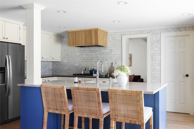 kitchen featuring stainless steel fridge, decorative backsplash, an island with sink, light wood-style floors, and a kitchen bar