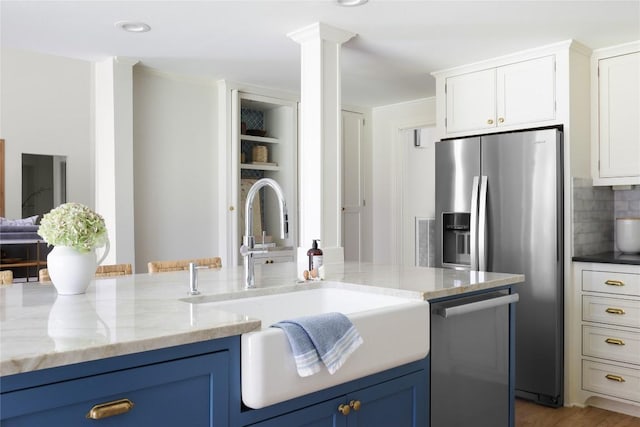 kitchen with light stone counters, blue cabinets, white cabinets, appliances with stainless steel finishes, and backsplash