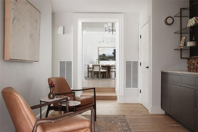 living area featuring light wood-style floors, visible vents, baseboards, and an inviting chandelier