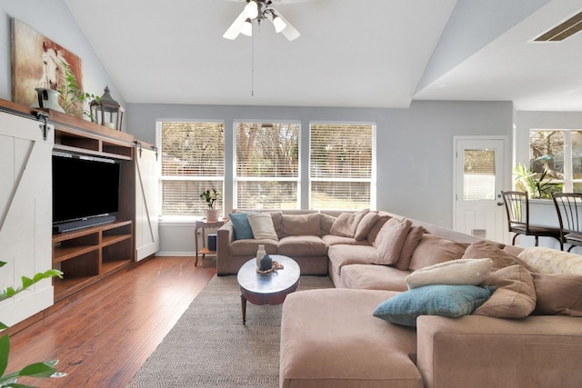 living area featuring lofted ceiling, a barn door, wood finished floors, visible vents, and a ceiling fan