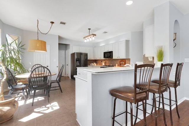 kitchen with black microwave, a peninsula, white cabinets, stainless steel fridge with ice dispenser, and tasteful backsplash