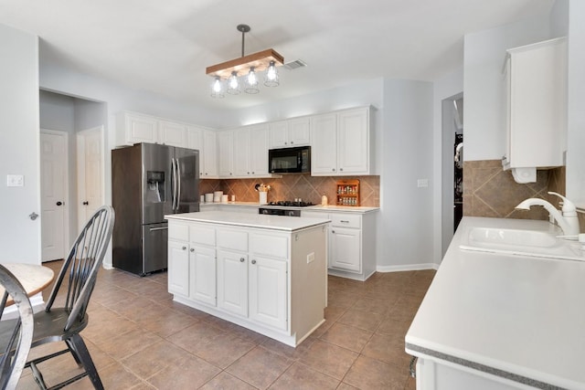 kitchen featuring black microwave, a sink, white cabinetry, light countertops, and stainless steel fridge