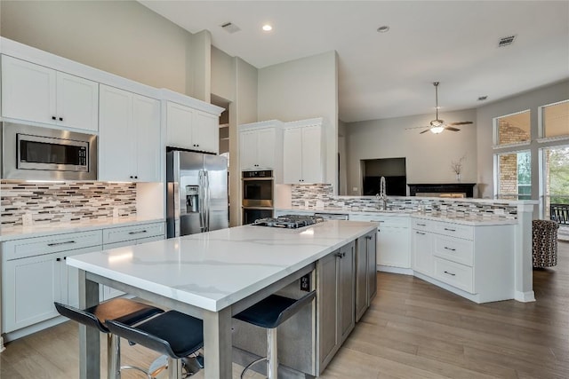 kitchen featuring a peninsula, a kitchen island, visible vents, white cabinets, and appliances with stainless steel finishes