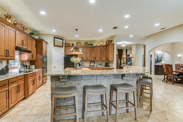 kitchen with arched walkways, a breakfast bar area, decorative backsplash, under cabinet range hood, and black appliances