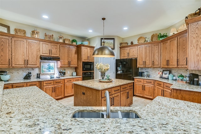 kitchen featuring light stone counters, backsplash, a sink, under cabinet range hood, and black appliances