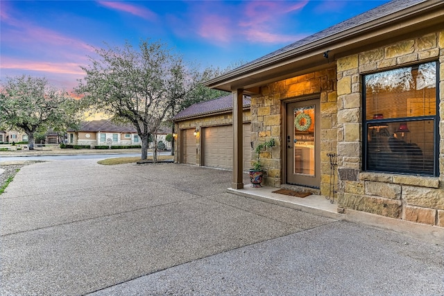 view of exterior entry with a garage, stone siding, and aphalt driveway