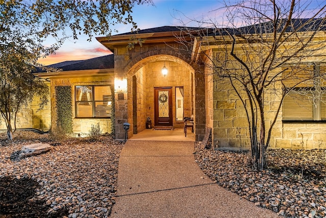 view of exterior entry featuring stone siding and roof with shingles