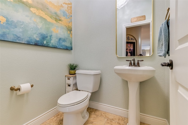 half bath with toilet, baseboards, and a sink