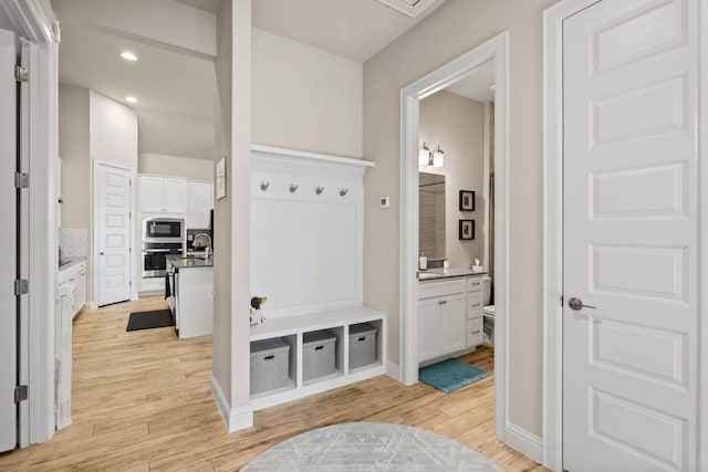 mudroom with light wood finished floors, baseboards, a sink, and recessed lighting