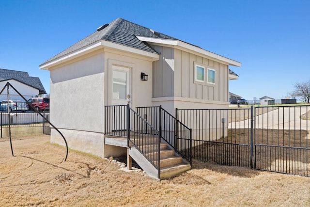 view of front facade with board and batten siding, roof with shingles, and fence