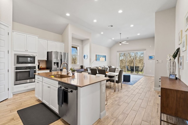 kitchen with stainless steel appliances, open floor plan, a sink, and light wood-style flooring