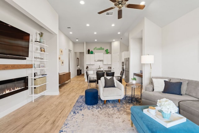 living room featuring recessed lighting, a ceiling fan, visible vents, light wood-style floors, and a glass covered fireplace