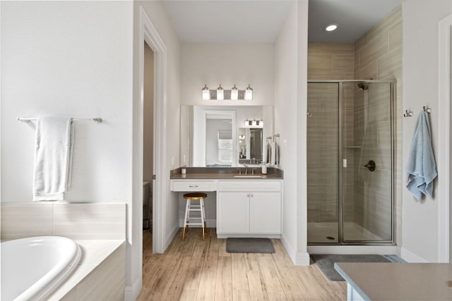 bathroom with wood finished floors, vanity, baseboards, a bath, and a stall shower