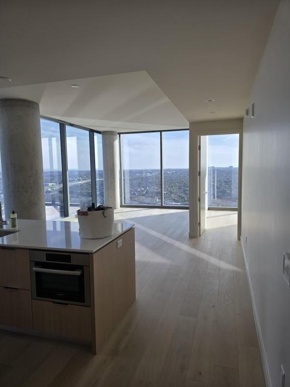 kitchen featuring baseboards, light wood-style flooring, modern cabinets, open floor plan, and oven