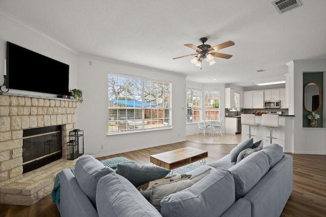 living room with a brick fireplace, visible vents, crown molding, and wood finished floors