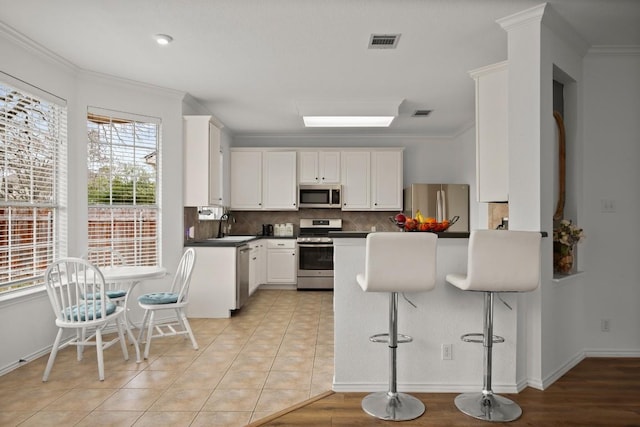 kitchen featuring appliances with stainless steel finishes, dark countertops, visible vents, and ornamental molding