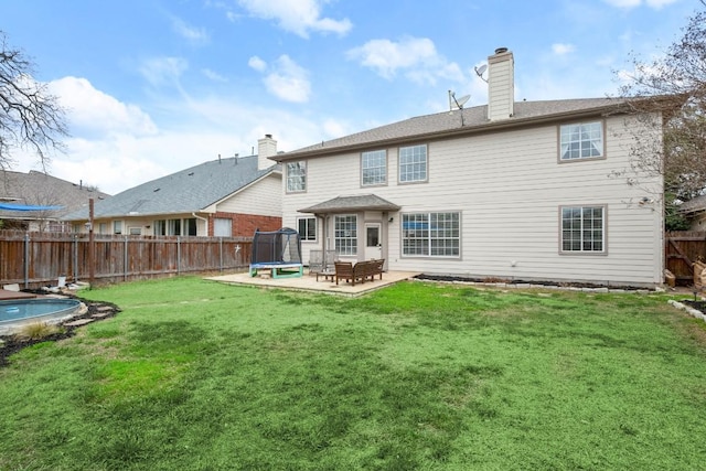 rear view of property featuring a fenced backyard, a chimney, a trampoline, a yard, and a patio area