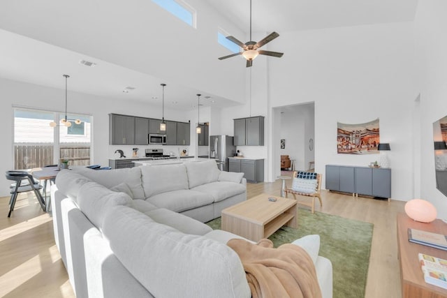 living area with visible vents, a towering ceiling, a ceiling fan, and light wood-style floors