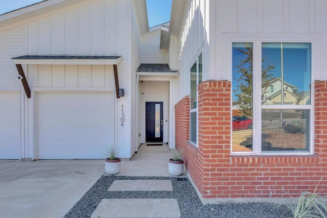 property entrance with driveway, a shingled roof, an attached garage, board and batten siding, and brick siding