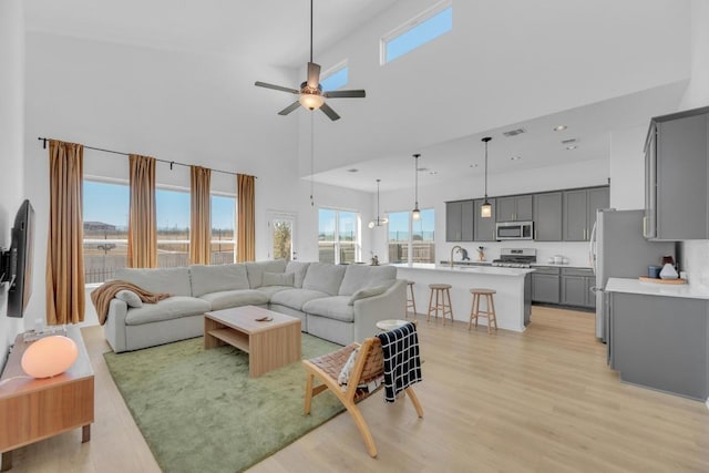 living area with visible vents, a towering ceiling, ceiling fan, light wood-style floors, and recessed lighting