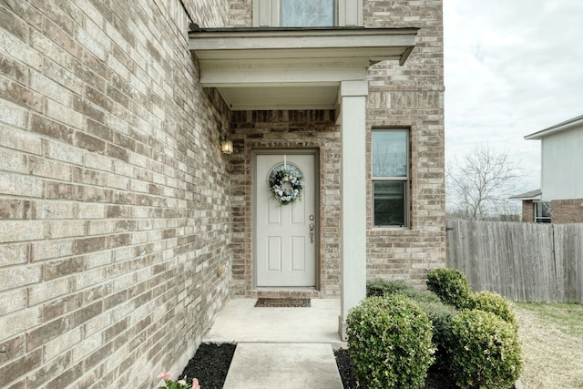 view of exterior entry with brick siding and fence