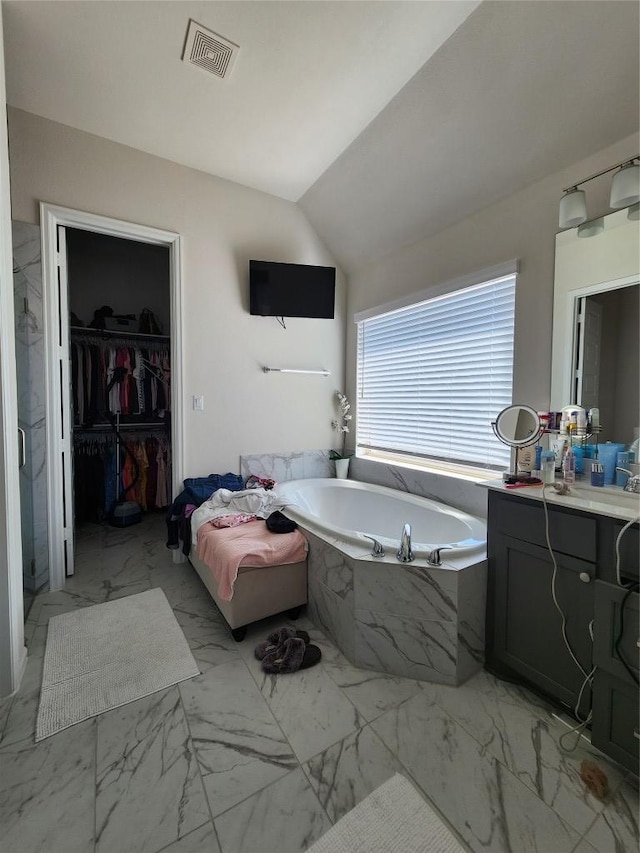 full bathroom with visible vents, a walk in closet, a bath, vanity, and vaulted ceiling