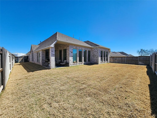 rear view of property with a patio, a fenced backyard, a shingled roof, a lawn, and brick siding