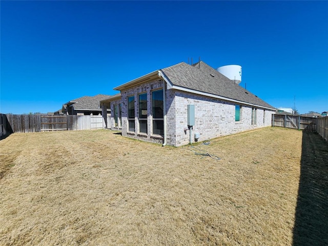 rear view of property with a yard, brick siding, a fenced backyard, and a shingled roof