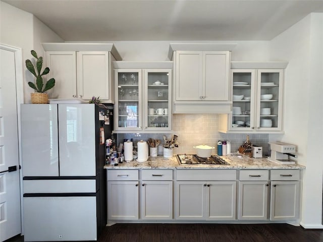 kitchen featuring light stone counters, backsplash, freestanding refrigerator, glass insert cabinets, and stainless steel gas cooktop