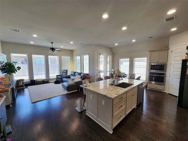 kitchen featuring visible vents, an island with sink, a sink, dark wood-style floors, and appliances with stainless steel finishes