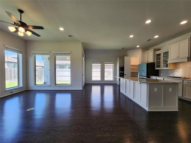 522 Jefferson Dr, Kyle, TX 78640 - kitchen with freestanding refrigerator, stainless steel gas cooktop, dark wood-style flooring, an island with sink, and light stone countertops