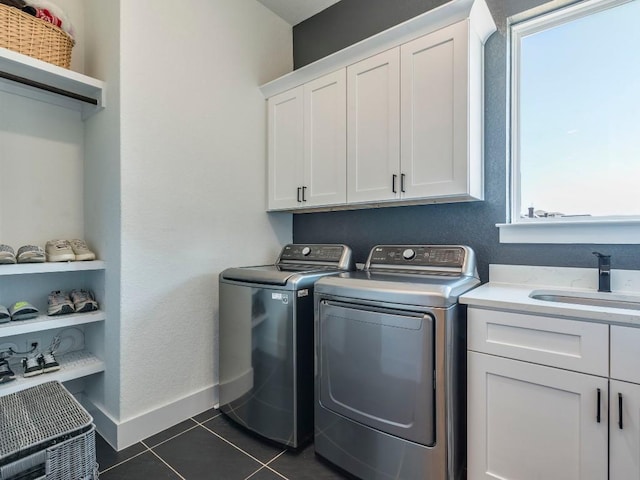 clothes washing area with cabinet space, baseboards, dark tile patterned flooring, washing machine and dryer, and a sink