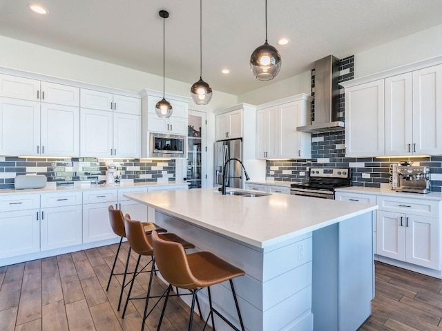 kitchen featuring a kitchen breakfast bar, dark wood-style flooring, stainless steel appliances, wall chimney range hood, and a sink